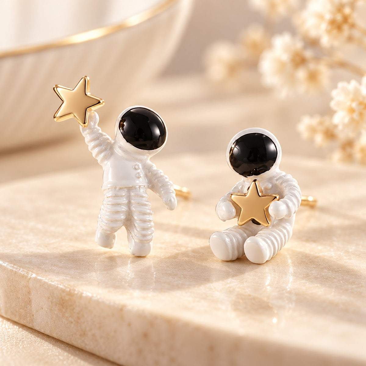 Mismatched astronaut stud earrings in white enamel with gold stars on marble