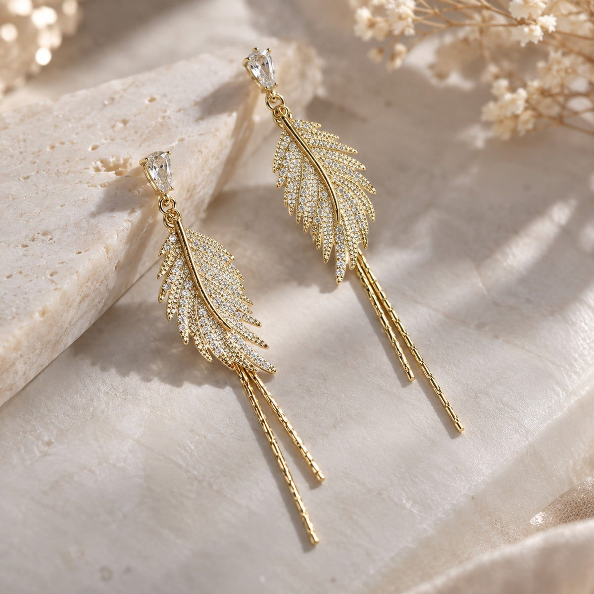 Pavé crystal gold feather earrings flat lay on marble
