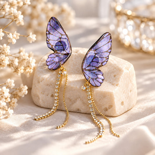 Purple butterfly wing earrings with gold rhinestone tassels on a stone display