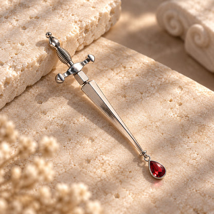 Silver dagger earring with red crystal teardrop lying on stone